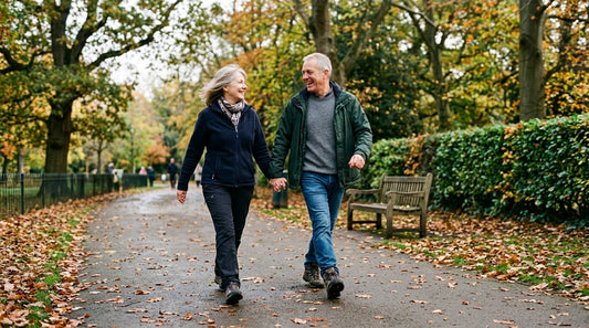 A couple in their late 50s taking a brisk walk together through a British park in autumn